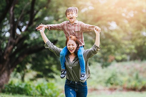 Child and Adolescent Behavioral Health Supports Coordination - mother carrying child on shoulders playfully - Encompass Community Supports