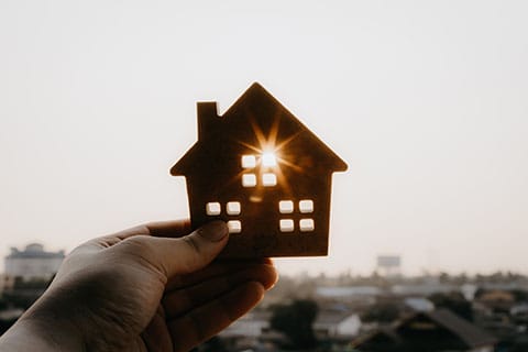 Housing Resources - image of hand holding wooden home cutout where sun shines through window - Encompass Community Supports