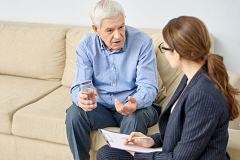 Quality of Care Supports - Long Term Ombudsman advocacy help - image of lady with notepad speaking with senior man - Encompass Community Supports