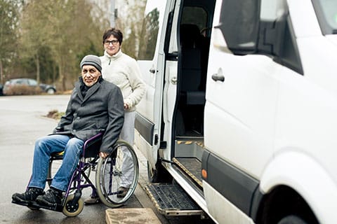 Local Transportation Support - a collaborative service with RTC Mobility Center - image of woman assisting man in wheelchair by a passenger van - Encompass Community Supports